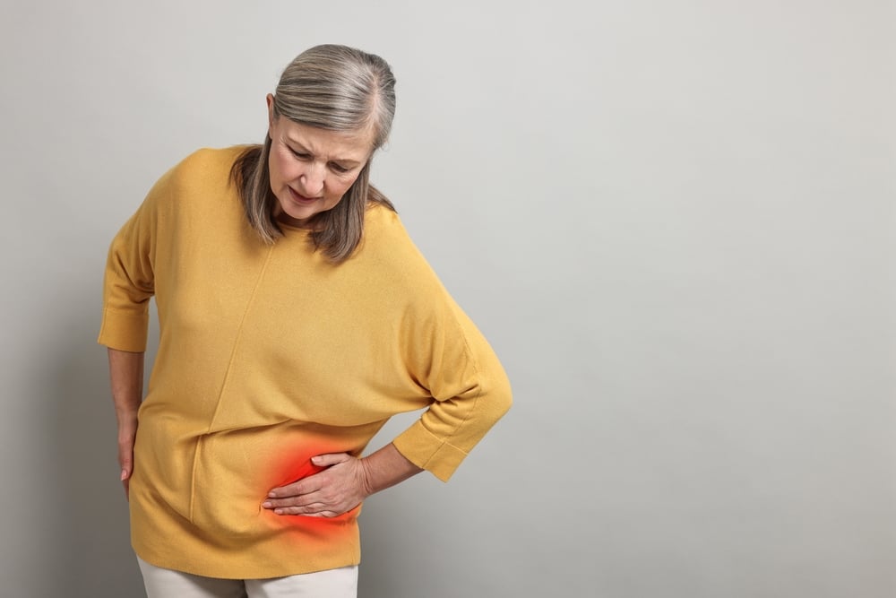 senior,woman,suffering,from,pain,in,hip,on,grey,background.